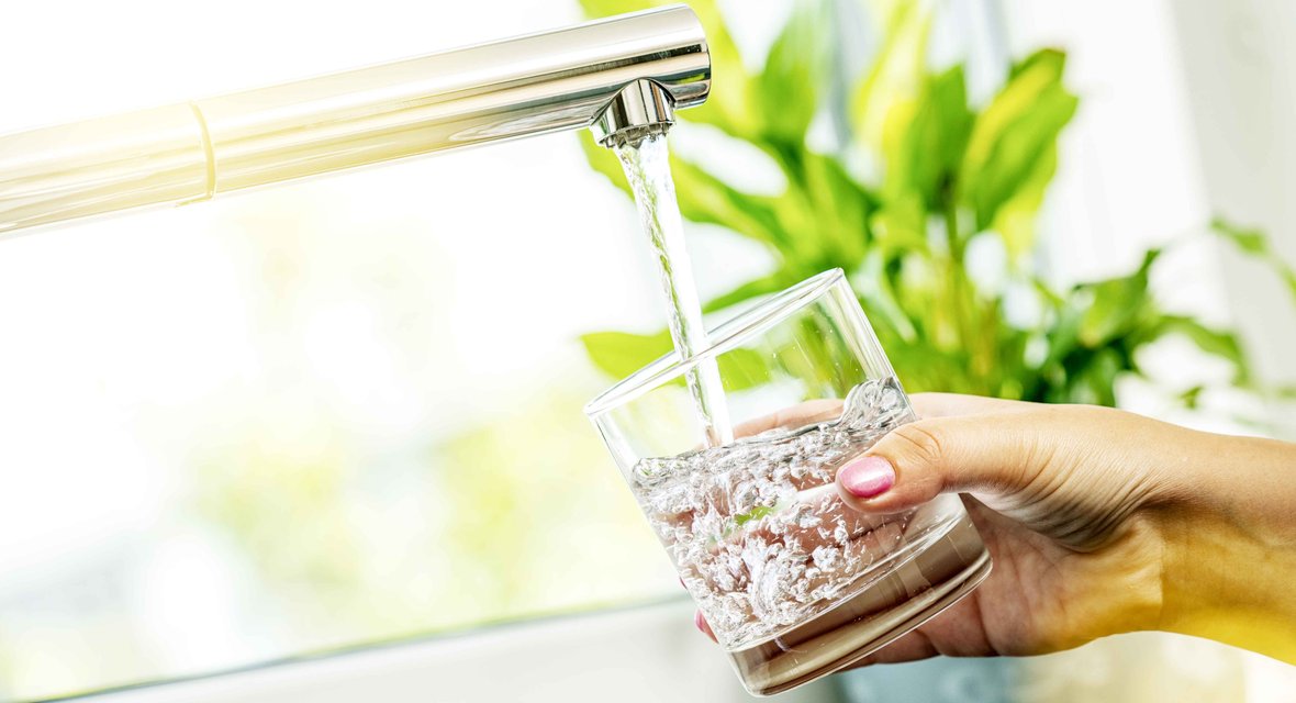 Symbolisches Bild mit Trinkglas wird am Wasserhahn mit Wasser gefüllt.